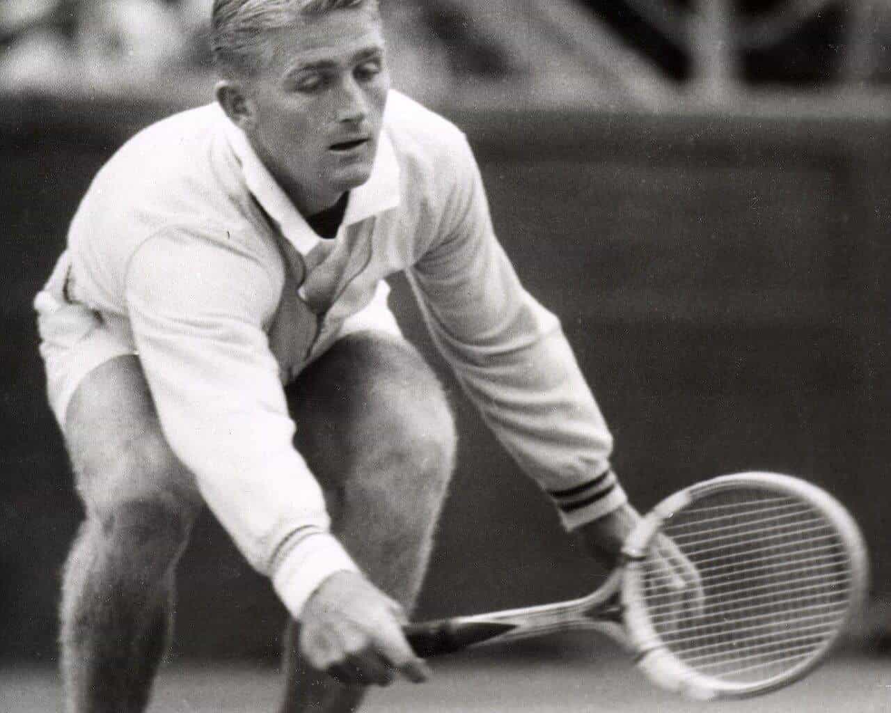 Lew Hoad crouching low to play a backhand on a grass court at Kooyong in 1954