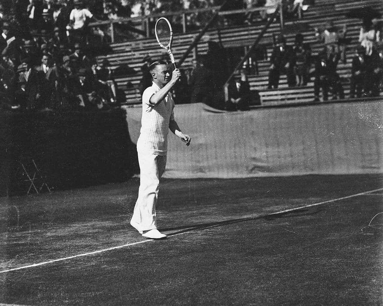 Harry Hopman playing a shot on a grass court in front of a crowd in 1931
