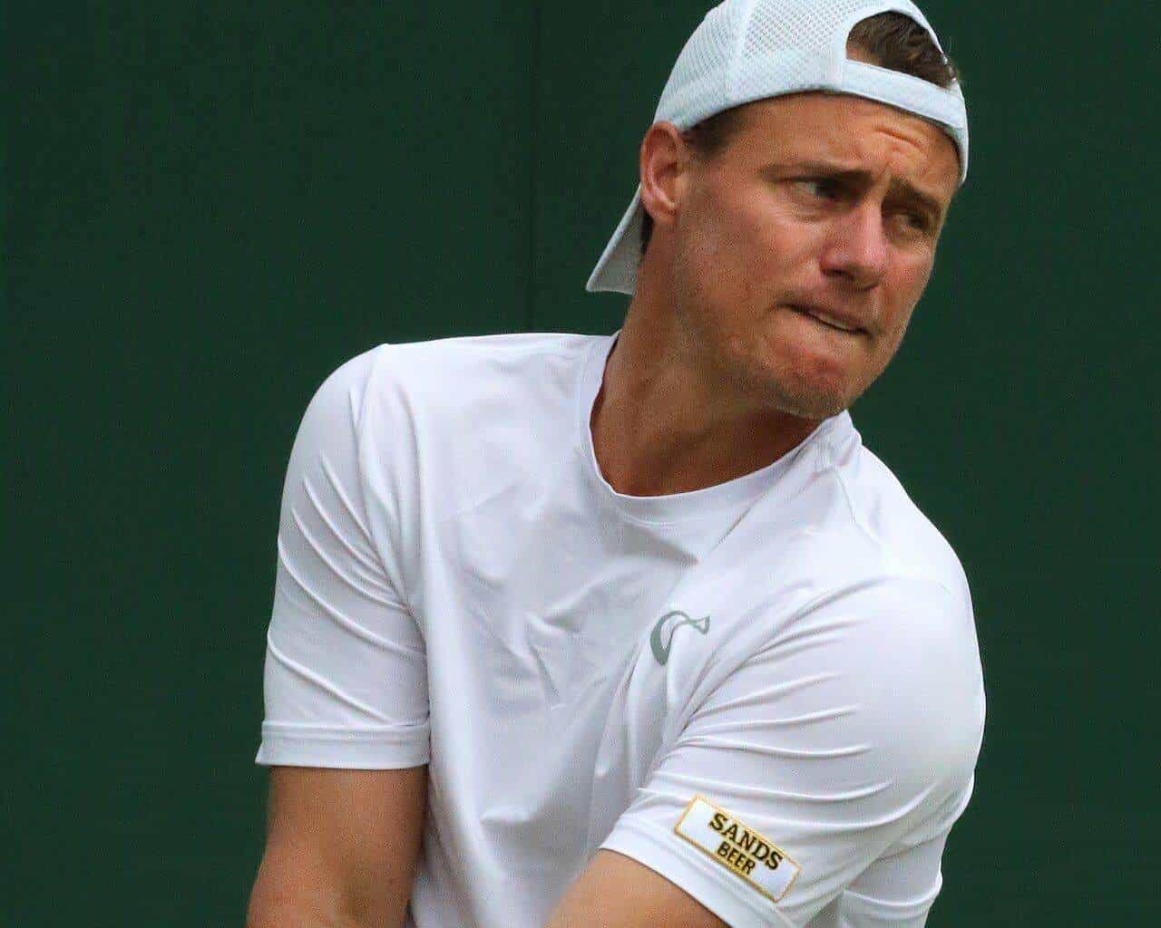 Lleyton Hewitt in a white cap and shirt preparing to serve on a grass court
